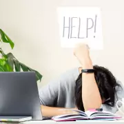 Frau mit Kopf auf Tisch und Help Schild hochhaltend