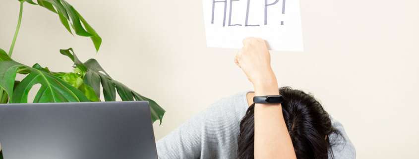 Frau mit Kopf auf Tisch und Help Schild hochhaltend