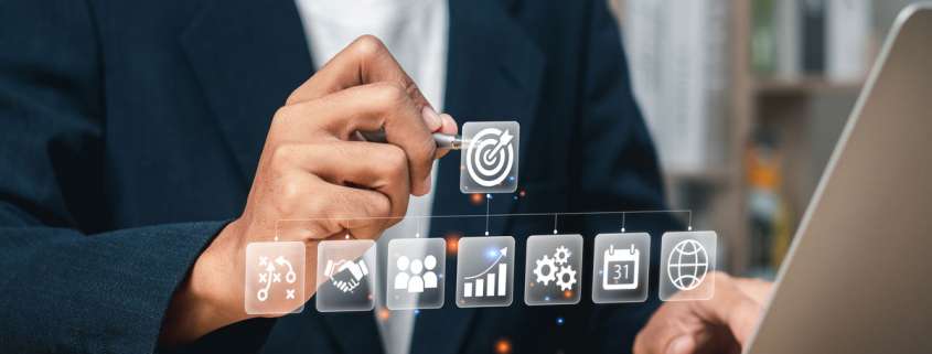 Mann vor Laptop tippt mit Stift auf Piktogramm Ziel